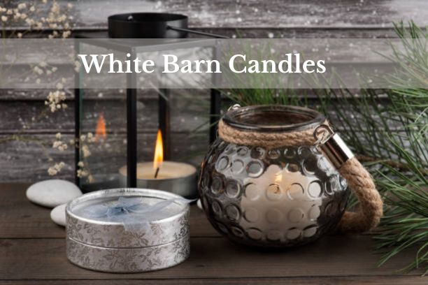 A beautifully lit White Barn Candle on a cozy table setting, creating a warm and inviting atmosphere.